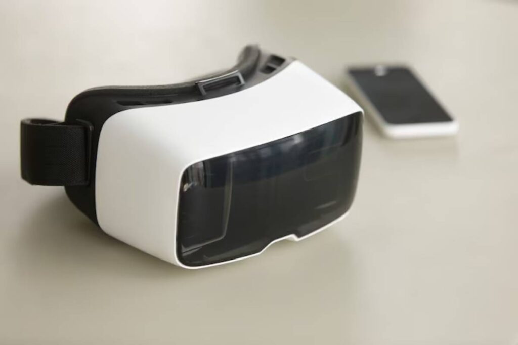 A white and black virtual reality headset rests on a light surface next to a black smartphone.