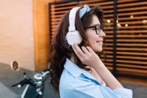 A person wears white headphones and a light blue shirt, enjoying music near a bicycle against a wooden-paneled background.