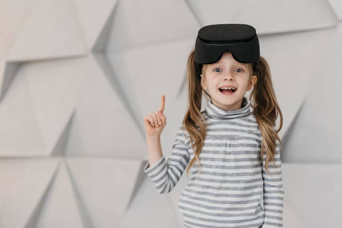 A child wearing virtual reality goggles, standing against a textured light gray wall, raises one finger in a thoughtful gesture.