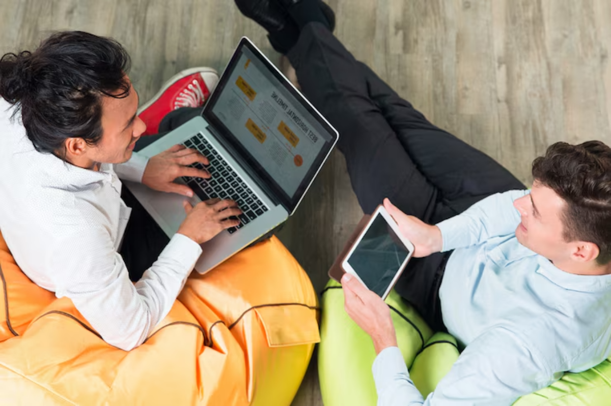 Two people sit on colorful bean bags, one using a laptop and the other holding a tablet, focused on their screens.