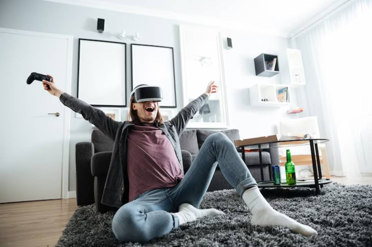 A person sits on the floor in a cozy living room wearing a VR headset, joyfully holding a game controller, with snacks and drinks nearby.