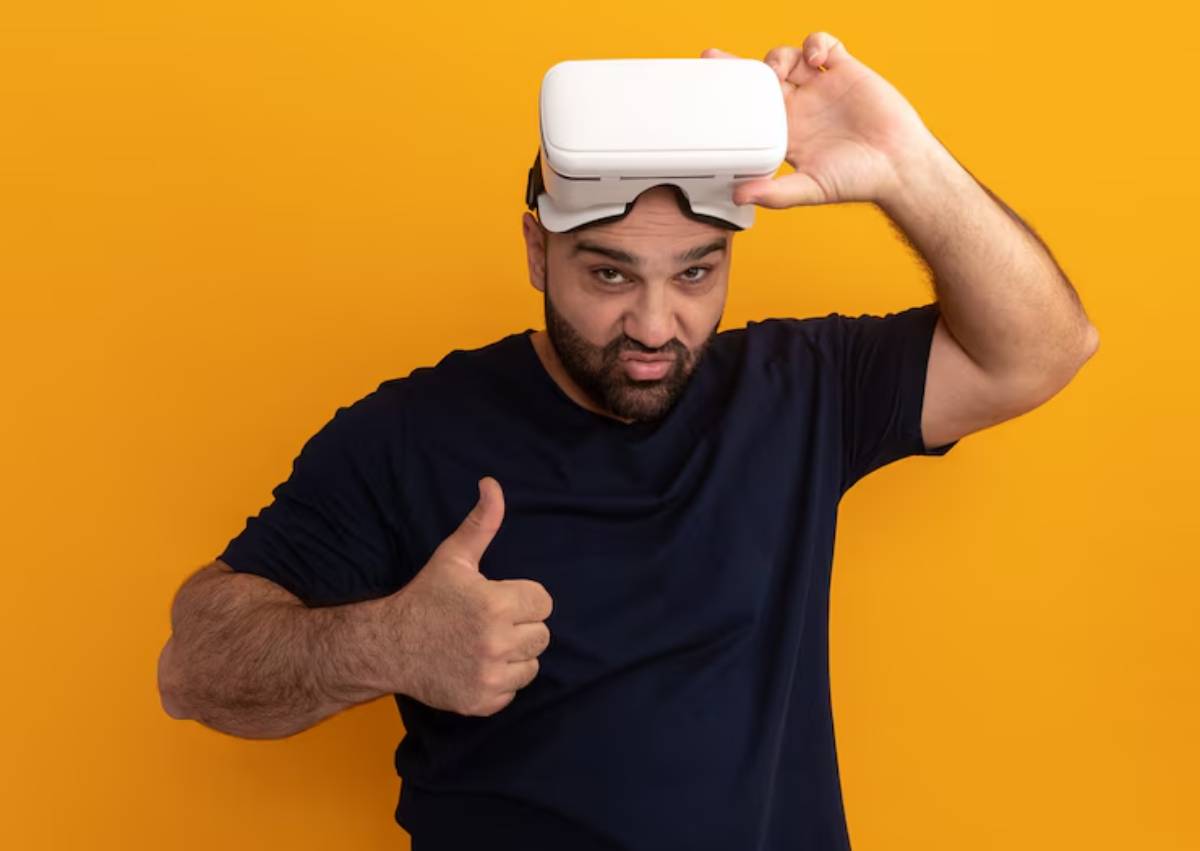 A person in a navy shirt holds a virtual reality headset and gives a thumbs-up against a bright orange backdrop.