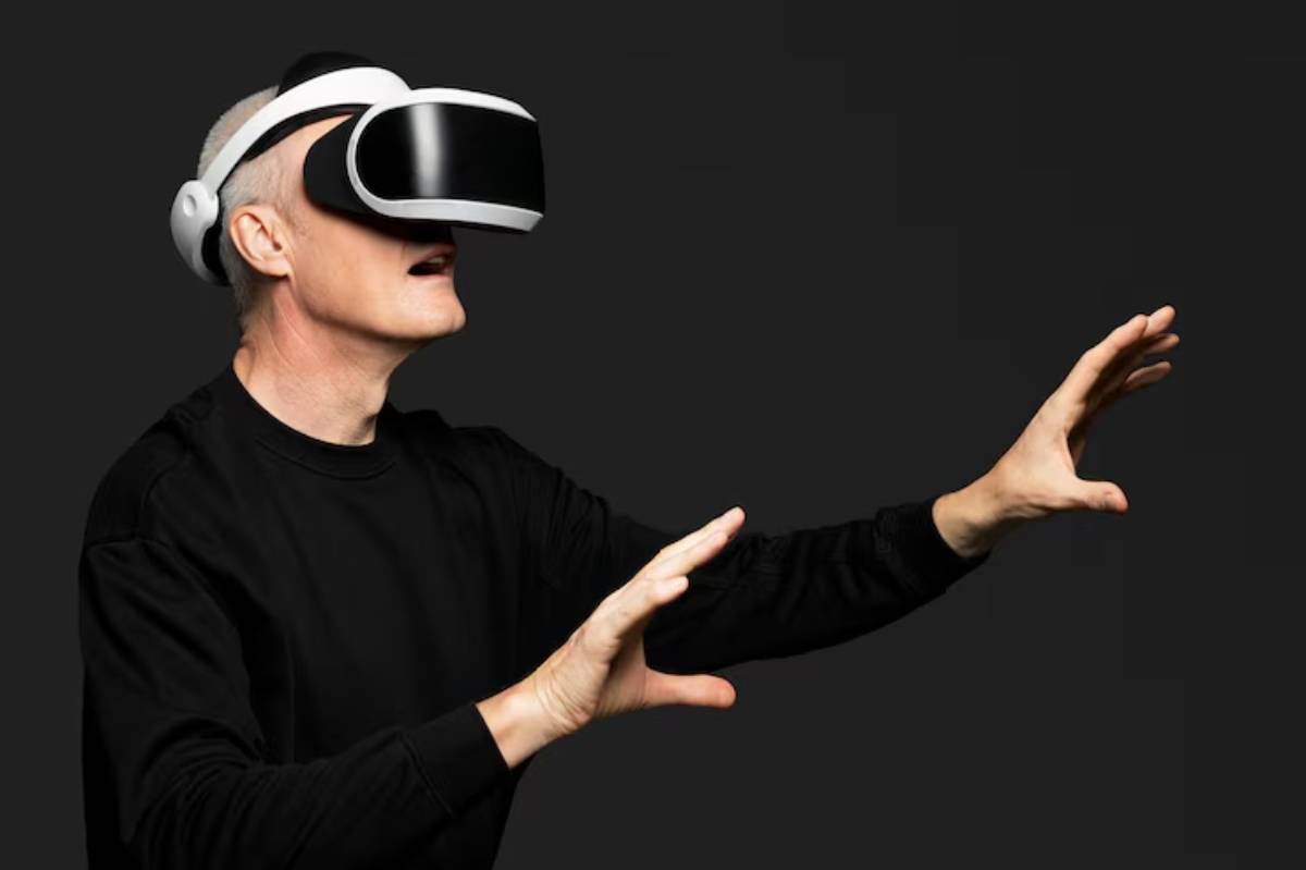 An elderly man wearing a virtual reality headset reaches out with his hands, engaging with an unseen digital environment.