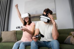 A woman wearing a VR headset joyfully raises her arm while a man beside her, also in a headset, looks contemplative, holding a controller.
