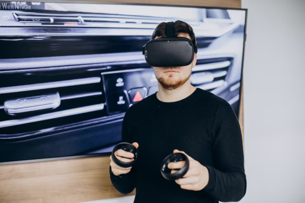 A person wearing a VR headset holds two controllers, standing in front of a large screen displaying car dashboard controls.