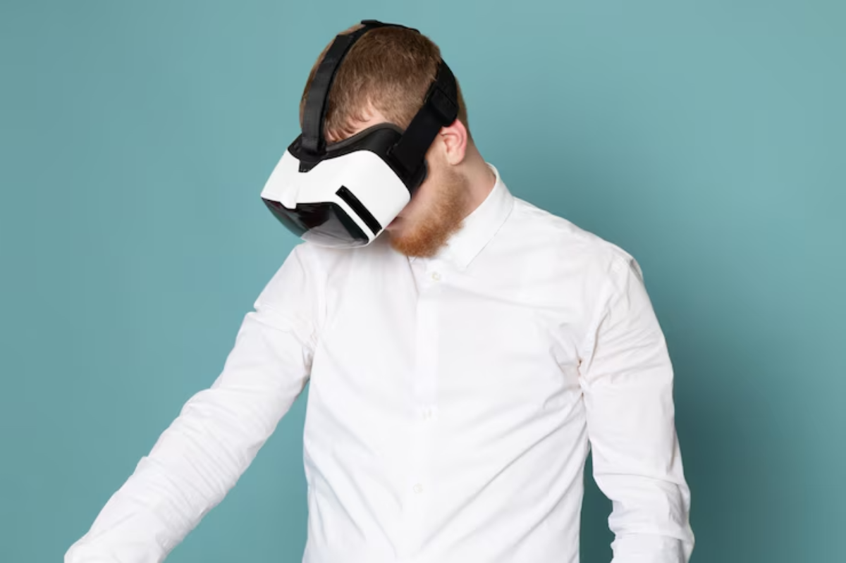 A man in a white shirt wears a virtual reality headset, looking down, set against a solid teal background.
