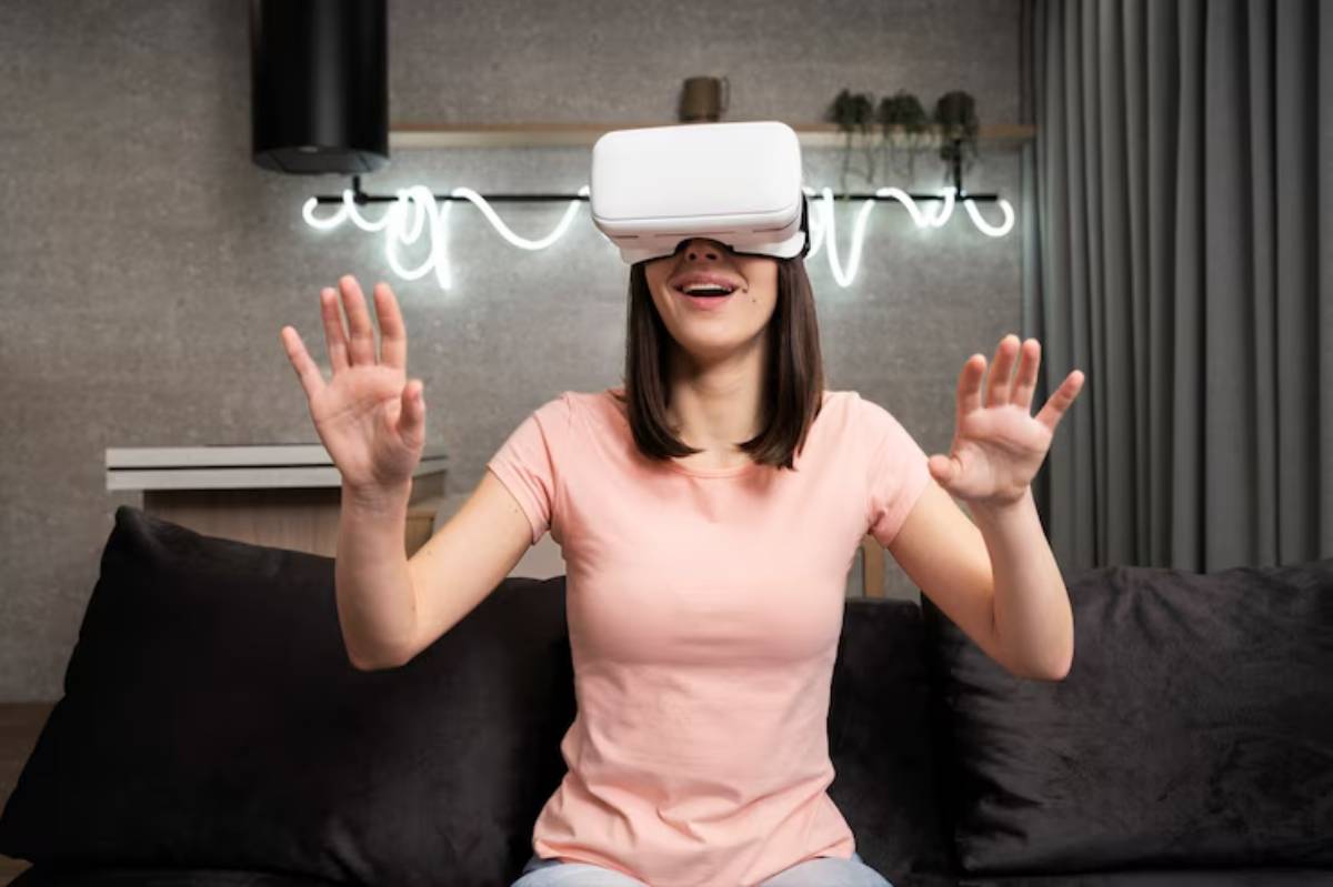 A woman wearing a virtual reality headset sits on a couch, gesturing with her hands as if interacting with a digital environment.