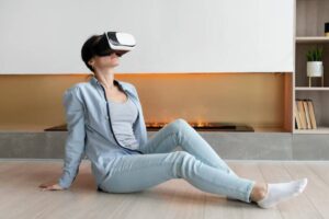 A person wearing a virtual reality headset sits on the floor in a modern, cozy living room with a warm fireplace in the background.