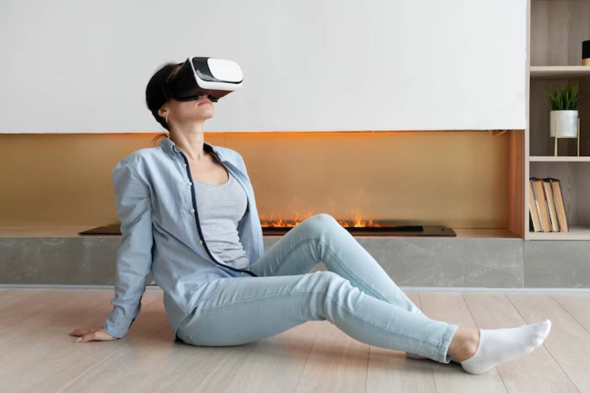 A person wearing a virtual reality headset sits on the floor in a modern, cozy living room with a warm fireplace in the background.