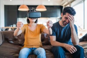 A person wearing a VR headset engages intensely on a sofa, while another individual beside them appears distressed or distracted.