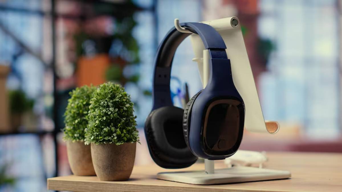 A pair of blue headphones displayed on a stand, beside two small potted plants on a wooden table, with a blurred background.