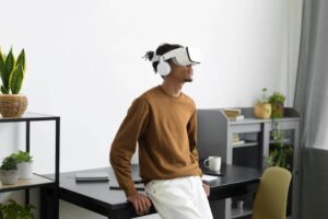 A person wearing a VR headset stands in a modern, minimalist workspace adorned with plants and a desk.