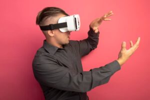 A person wearing a virtual reality headset gestures enthusiastically against a bright pink background.