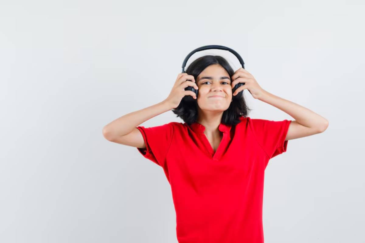 A person in a red polo shirt wears headphones, holding them with both hands, against a plain white background.