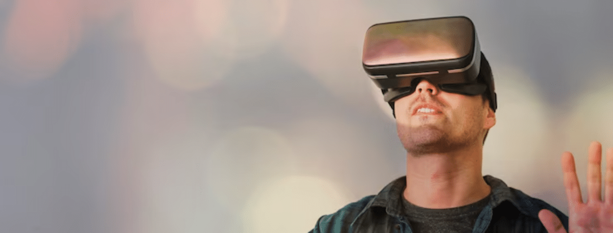 A person wearing a virtual reality headset raises their hand, immersed in a digital experience against a blurred, colorful background.