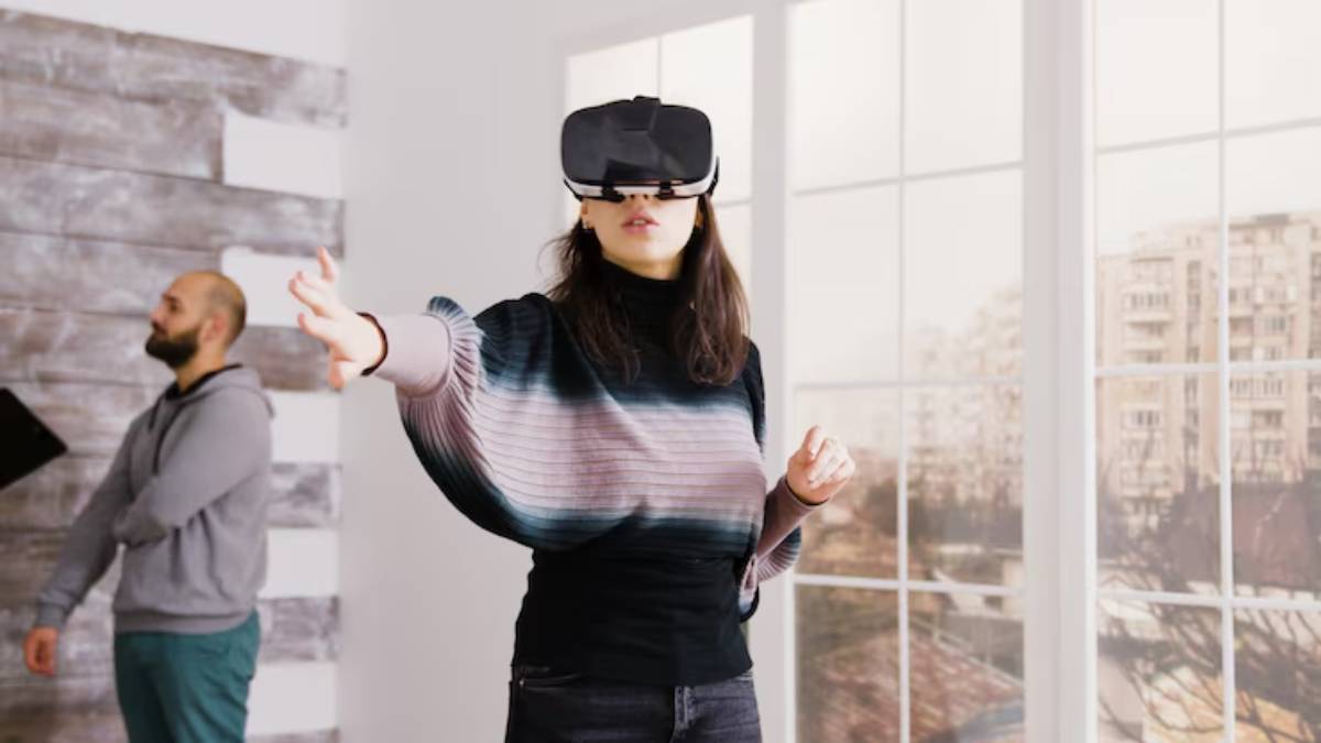 A person wearing a virtual reality headset gestures playfully in a bright room with large windows and wooden decor.