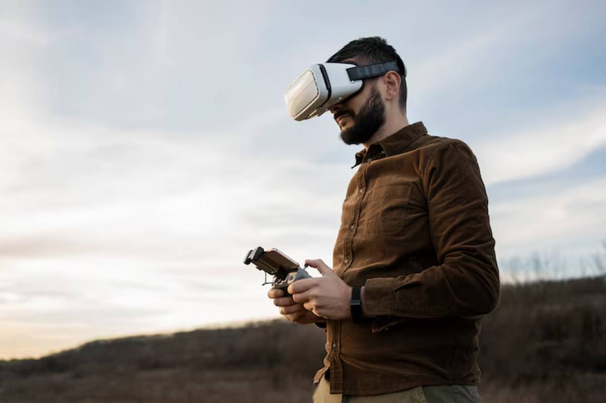 A person wearing virtual reality goggles holds a drone controller outdoors, with a scenic landscape and cloudy sky in the background.