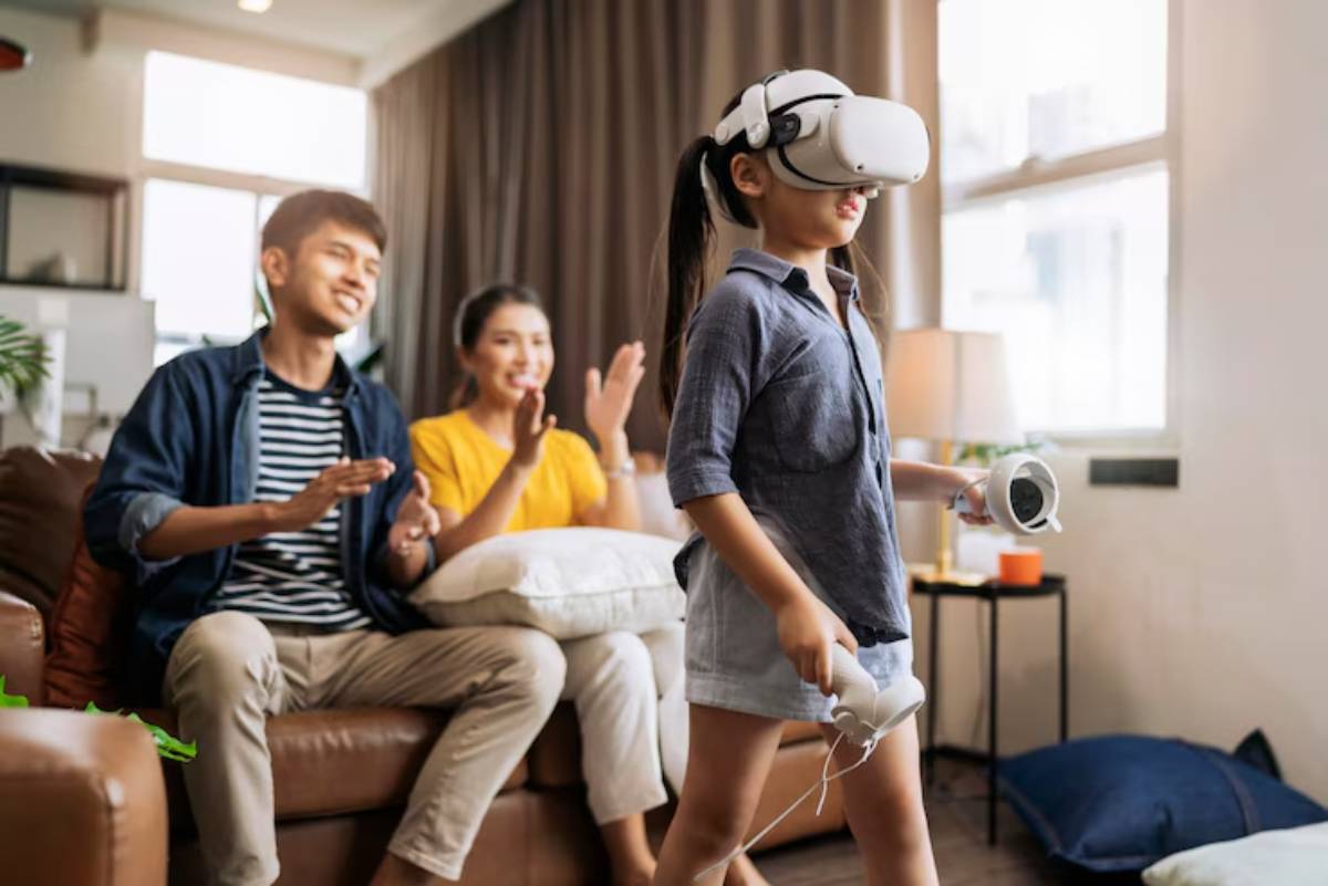 A young girl in a VR headset holds controllers while two friends cheer her on from a cozy living room couch.
