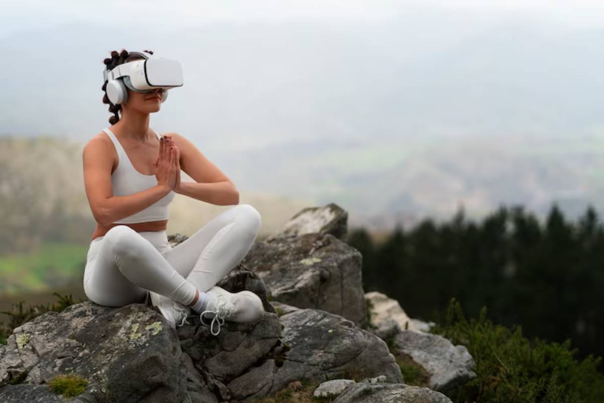 A person in white athletic wear practicing yoga meditation on rocky terrain, surrounded by a lush mountainous landscape.