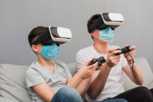 A child and an adult sit on a gray couch, both wearing virtual reality headsets and holding video game controllers, fully engaged in gaming.