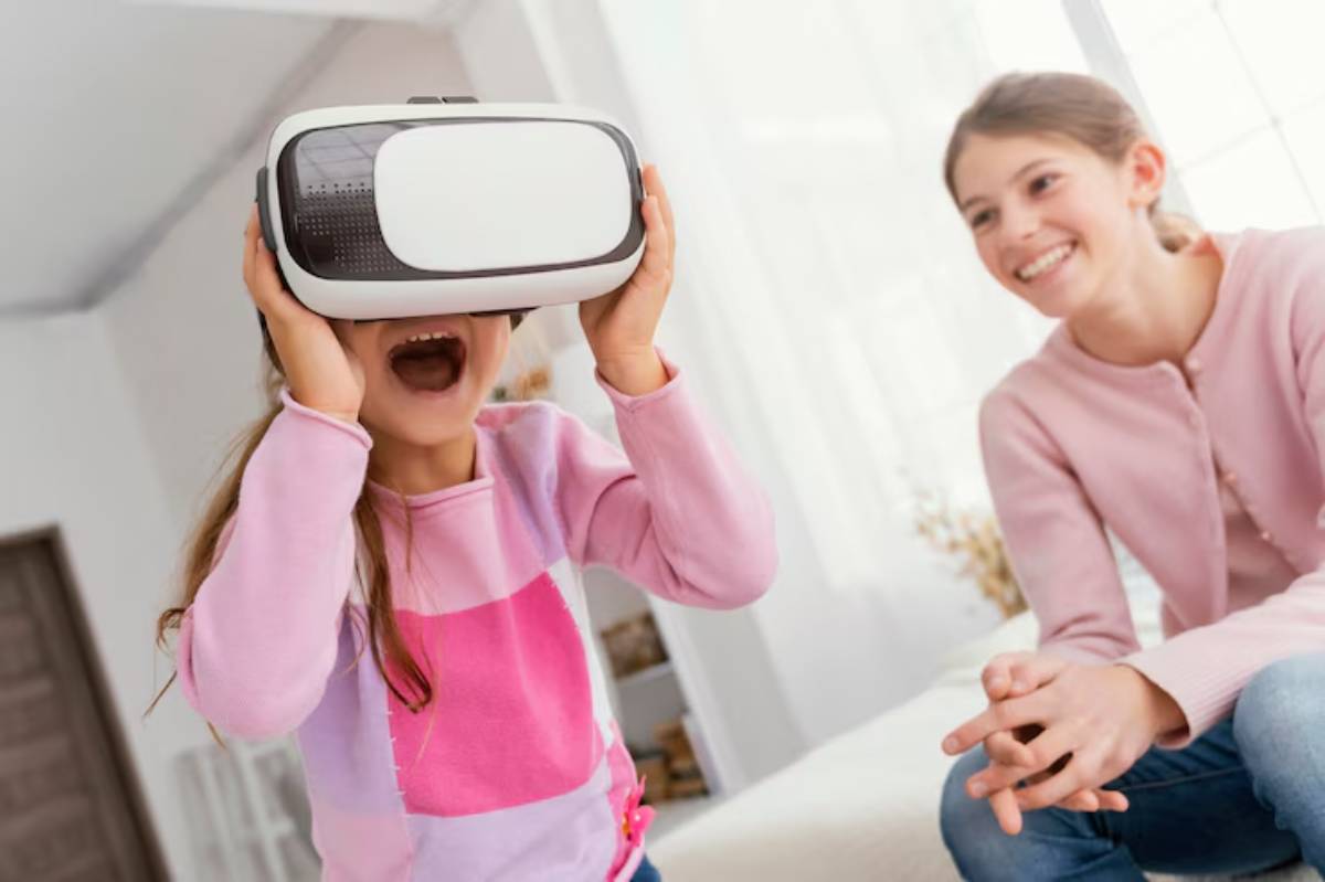 A child wearing a virtual reality headset is immersed in an experience, while another seated girl observes curiously in a bright room.
