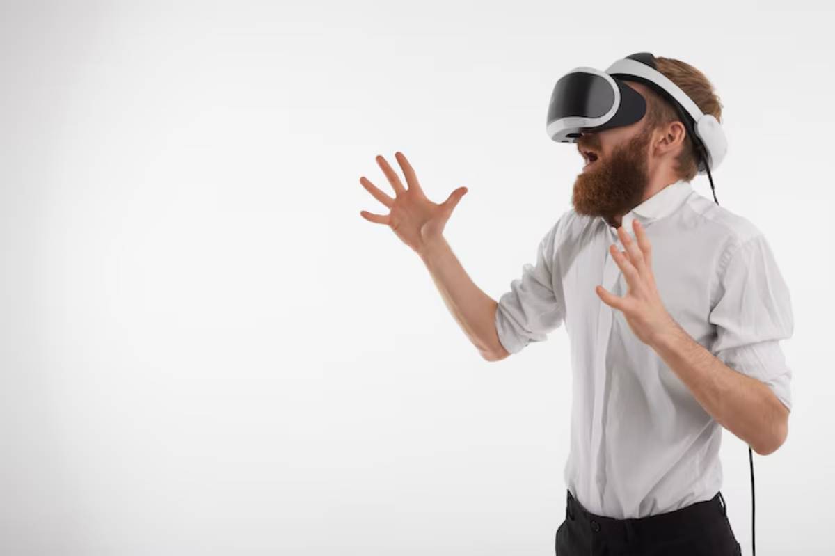 A man in a white shirt wearing a VR headset gestures excitedly, immersed in a virtual experience against a plain background.